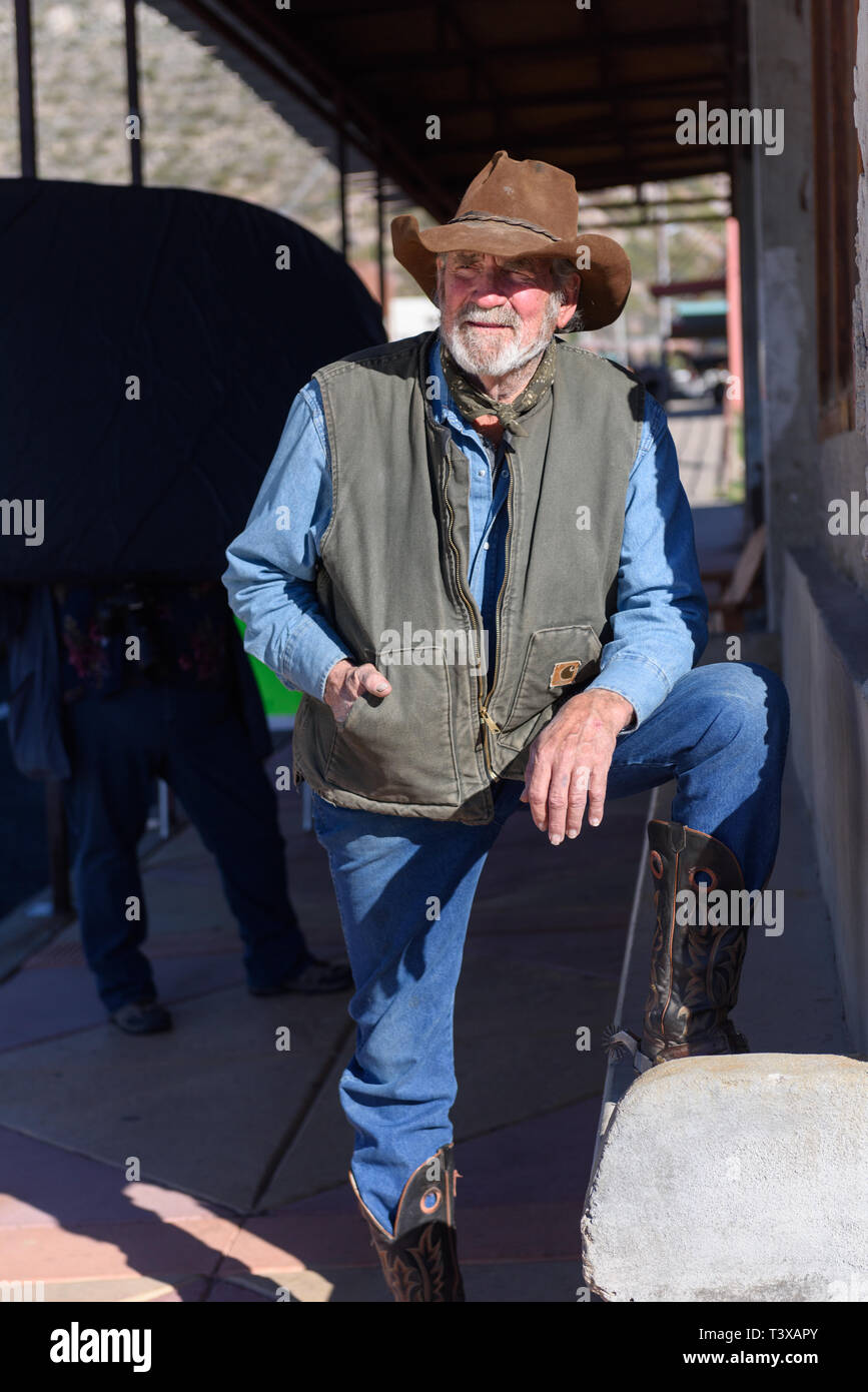 Old cowboy porte des bottes de cow-boy qui sont brunes avec conception cousu sur le côté, un jean bleu et un chapeau de cowboy en cuir poussiéreux. Banque D'Images