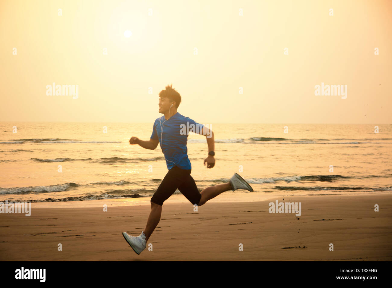 Jeune homme qui court sur la plage au coucher du soleil Banque D'Images