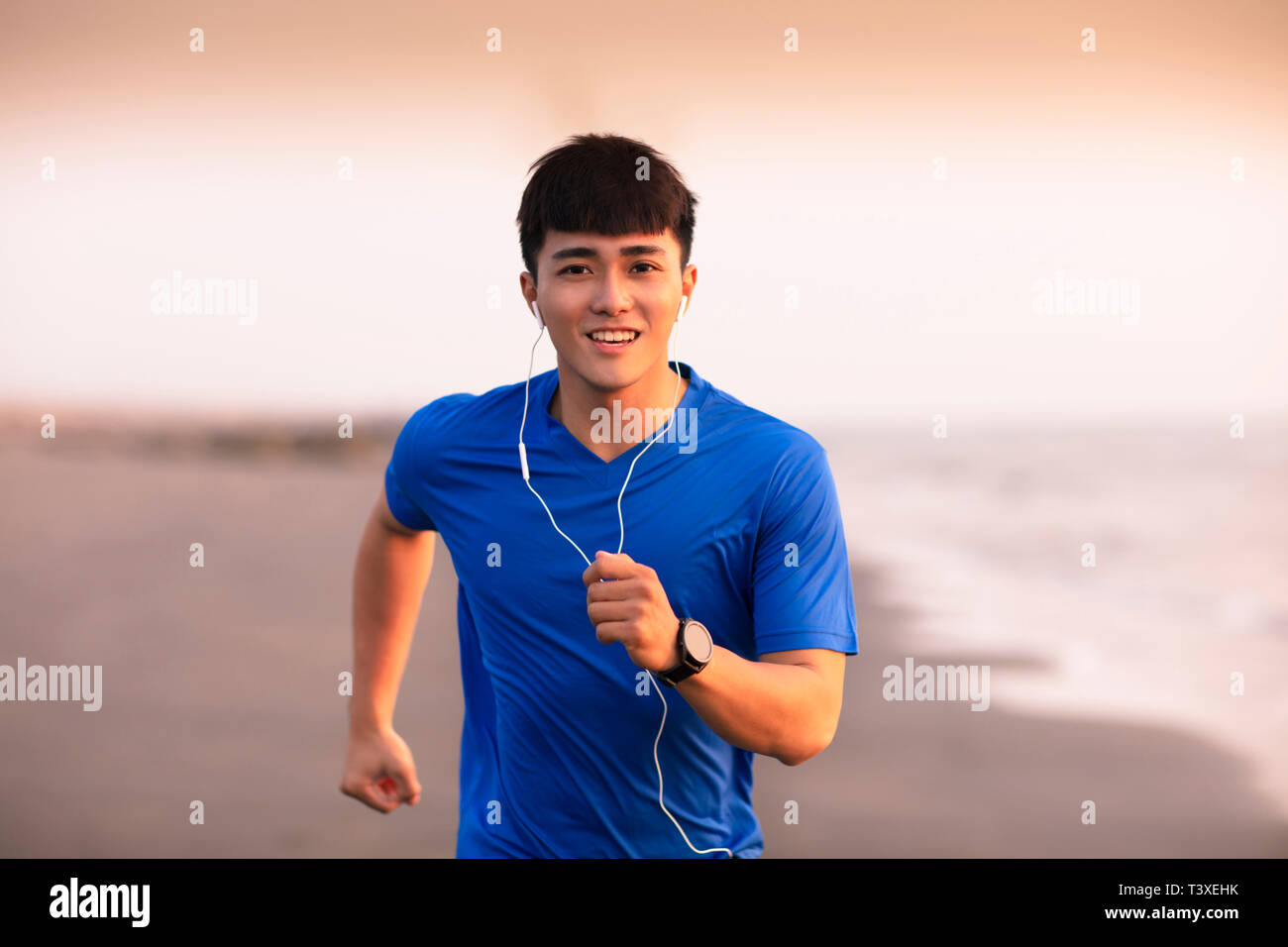 Jeune homme qui court sur la plage au coucher du soleil Banque D'Images