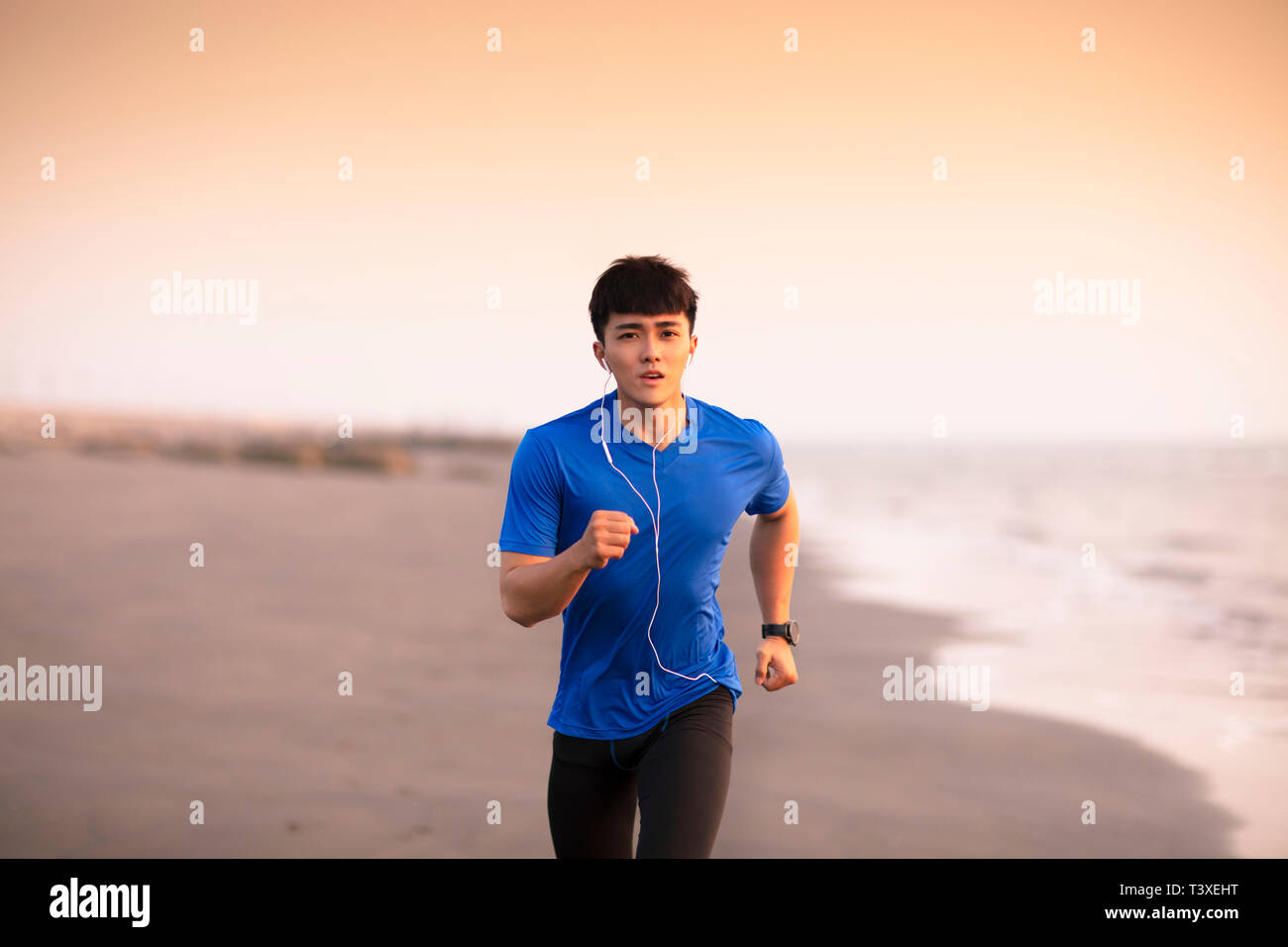 Jeune homme qui court sur la plage au coucher du soleil Banque D'Images