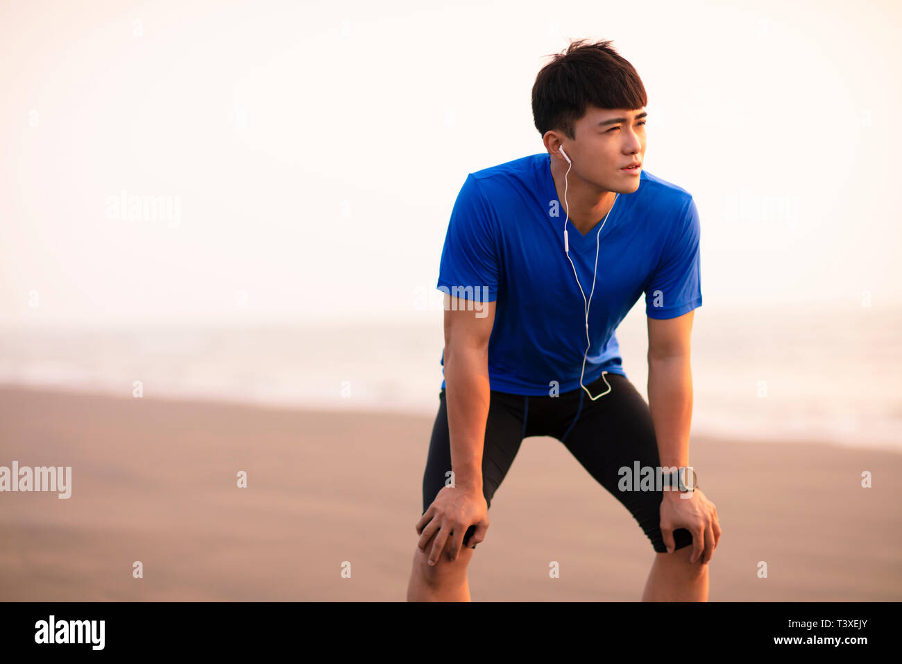 Jeune homme prendre de pause après l'exécution sur la plage au coucher du soleil Banque D'Images