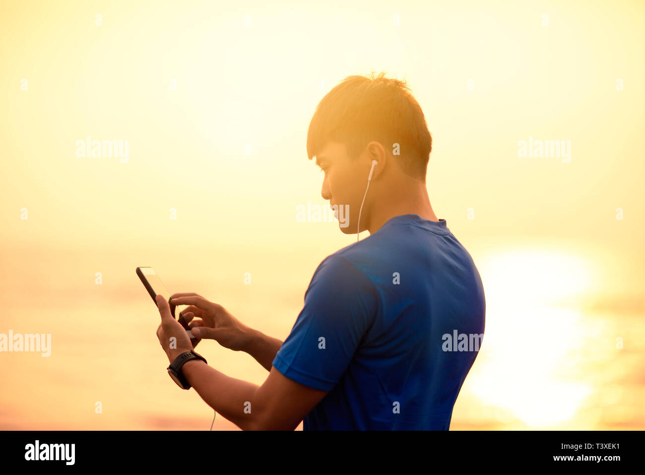Jeune homme d'exécution sur plage et contrôle de moniteur de fréquence cardiaque sur smart phone Banque D'Images
