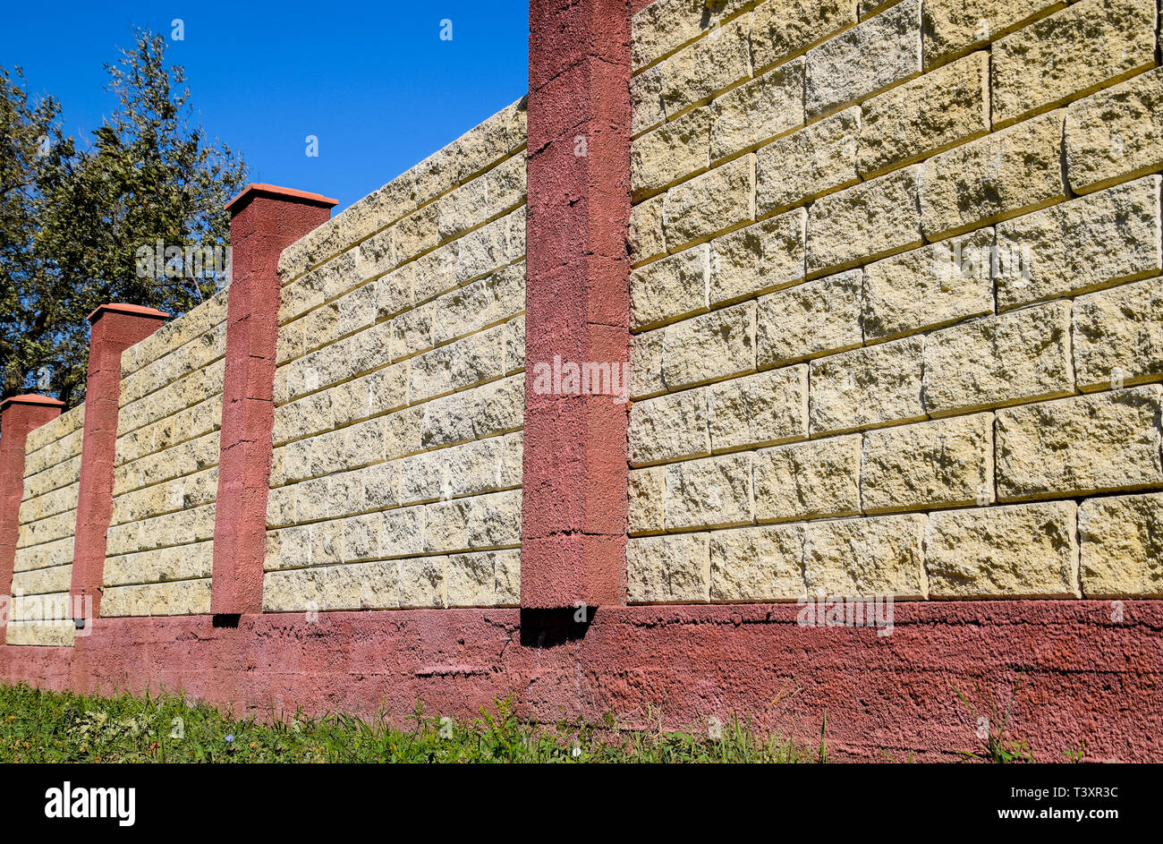 Clôture faite de briques et de plâtre décoratif. Clôture jaune rouge avec éléments. L'escrime de haut et beau. Banque D'Images
