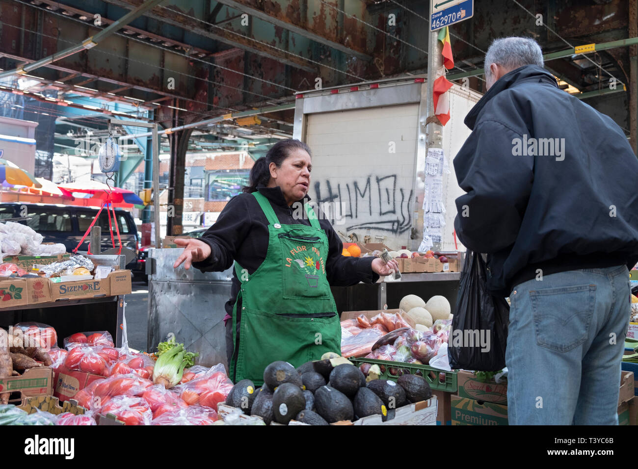 Une femme hispanique parle à un client à son stand de fruits et légumes sur Roosevelt Ave & Warren Street à Corona, Queens, New York. Banque D'Images