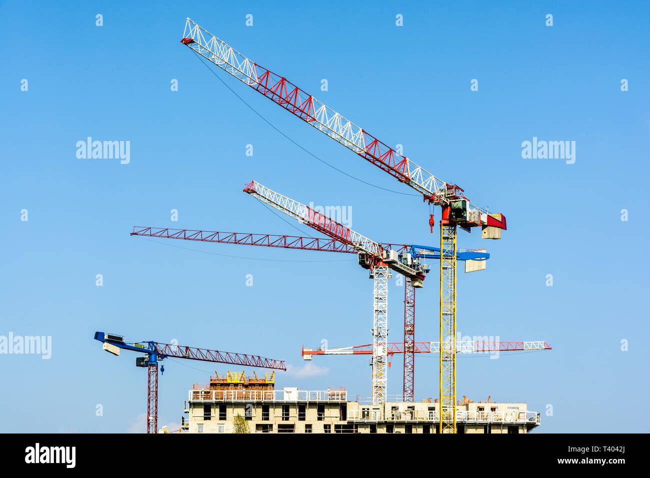 Cinq grandes grues à tour au-dessus d'un bâtiment en construction en béton contre le ciel bleu. Banque D'Images
