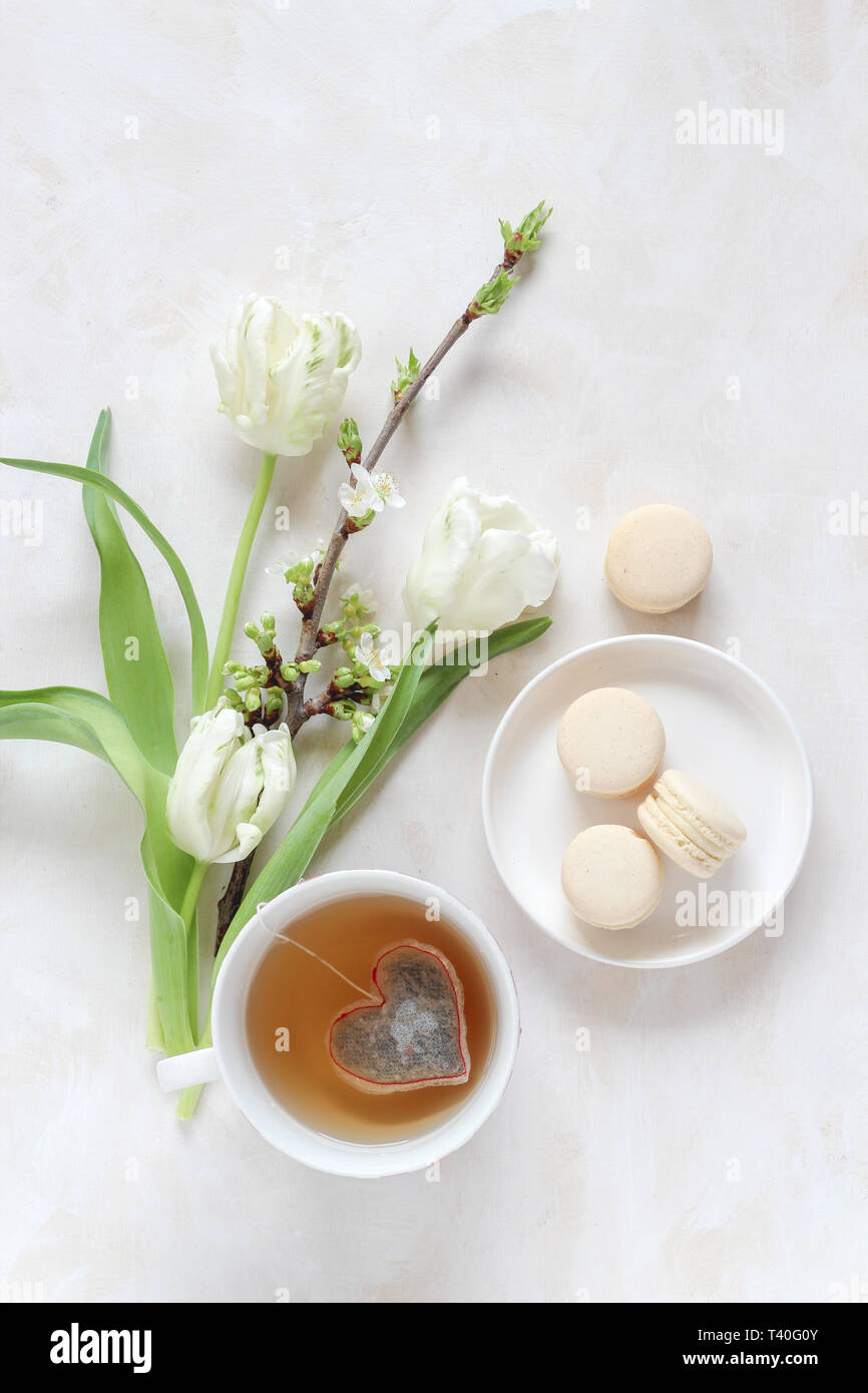 Fleurs de printemps et d'une tasse de thé avec un sachet de thé en forme de coeur et macarons sur un arrière-plan lumineux, télévision jeter style avec un copy space Banque D'Images