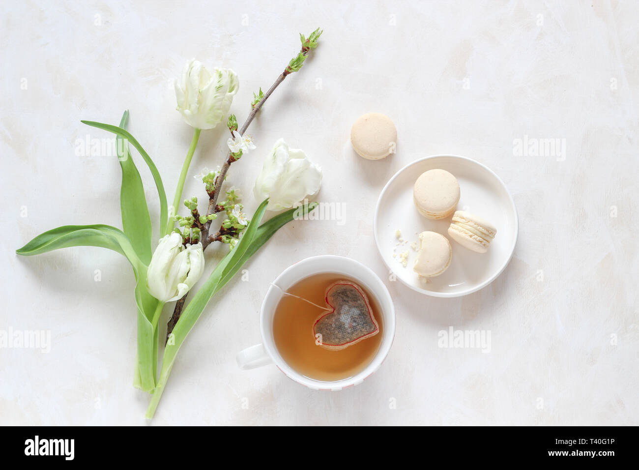 Fleurs de printemps et d'une tasse de thé avec un sachet de thé en forme de coeur et macarons sur un arrière-plan lumineux, télévision jeter style avec un copy space Banque D'Images
