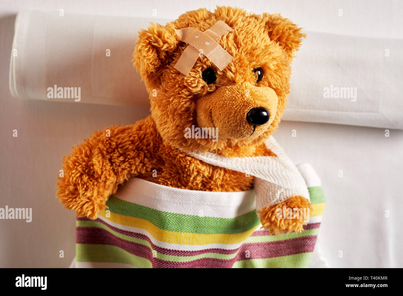 Mignon petit ours en peluche avec un bras en écharpe et le plâtre ou un  bandage sur sa tête au lit sous une couverture colorée dans un concept de  medi pédiatrique Photo
