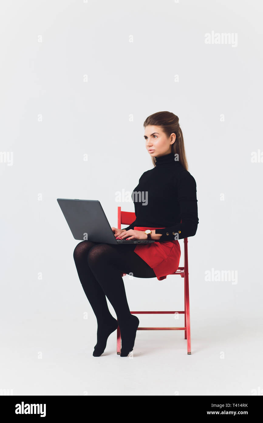 Photo de belle femme 20s le sourire et à l'aide d'ordinateur avec les jambes croisés isolated over white background. Banque D'Images
