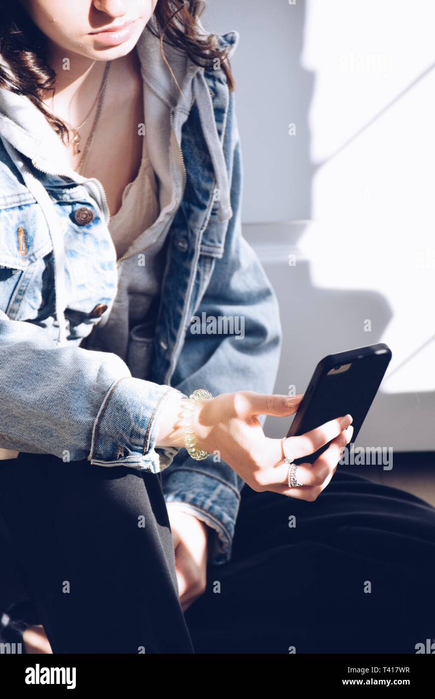 Adolescente assis sur le plancher à l'aide d'un téléphone mobile Banque D'Images