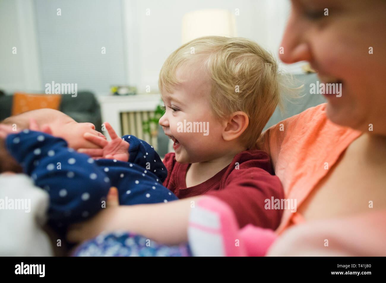 Heureux adorable garçon blond met bras autour de bébé assis avec maman Banque D'Images