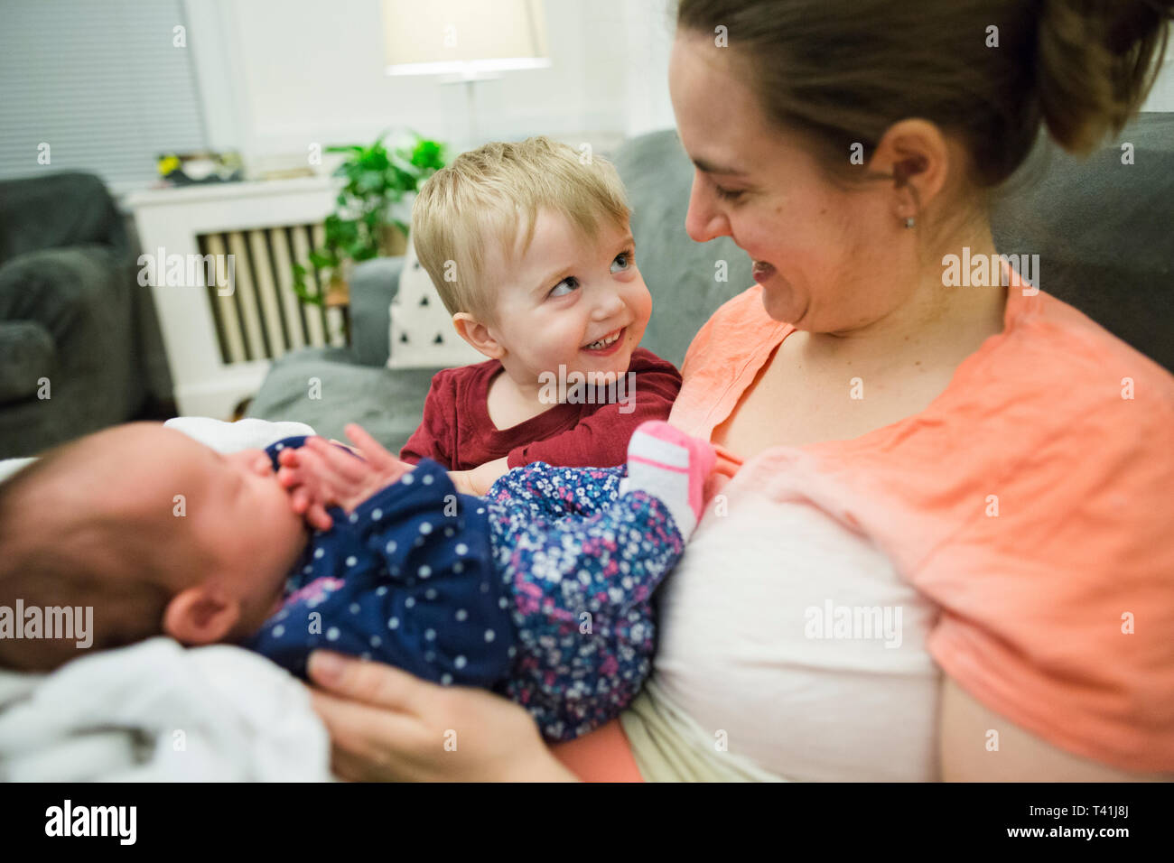 Happy blonde bébé garçon regarde mother holding newborn baby girl Banque D'Images