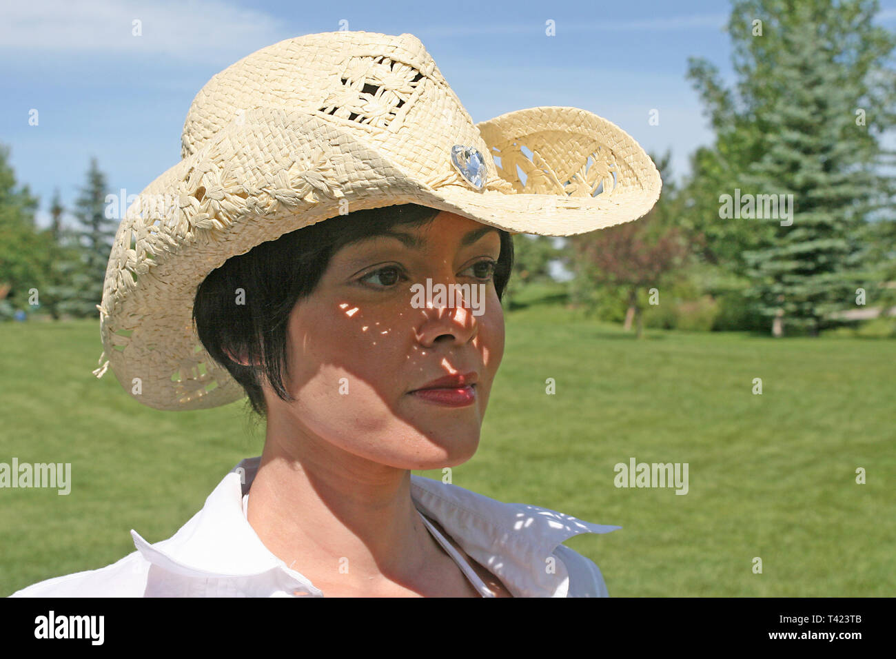 Dark haired woman posing in a park portant un chapeau de paille Banque D'Images