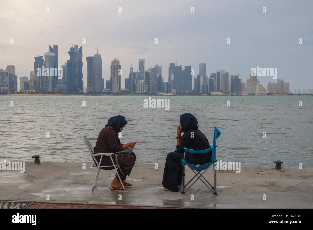 Doha, Qatar. 13 avr, 2019. Deux femmes profiter assis sur le bord de mer avec une vue sur la Corniche de gratte-ciel après une matinée pluvieuse et humide dans le capital Crédit : amer ghazzal/Alamy Live News Banque D'Images