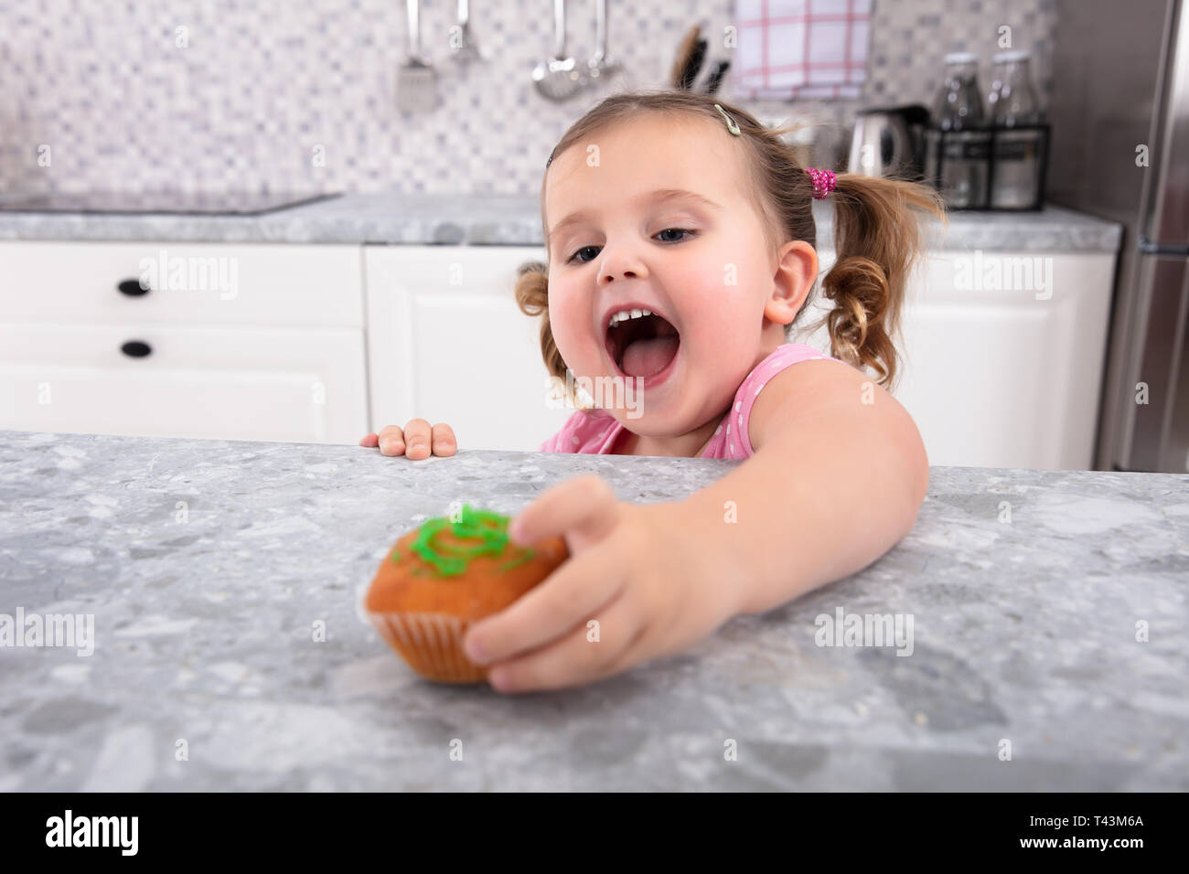 Smiling cute girl's Hand Reaching For Cupcake sur compteur de cuisine Banque D'Images