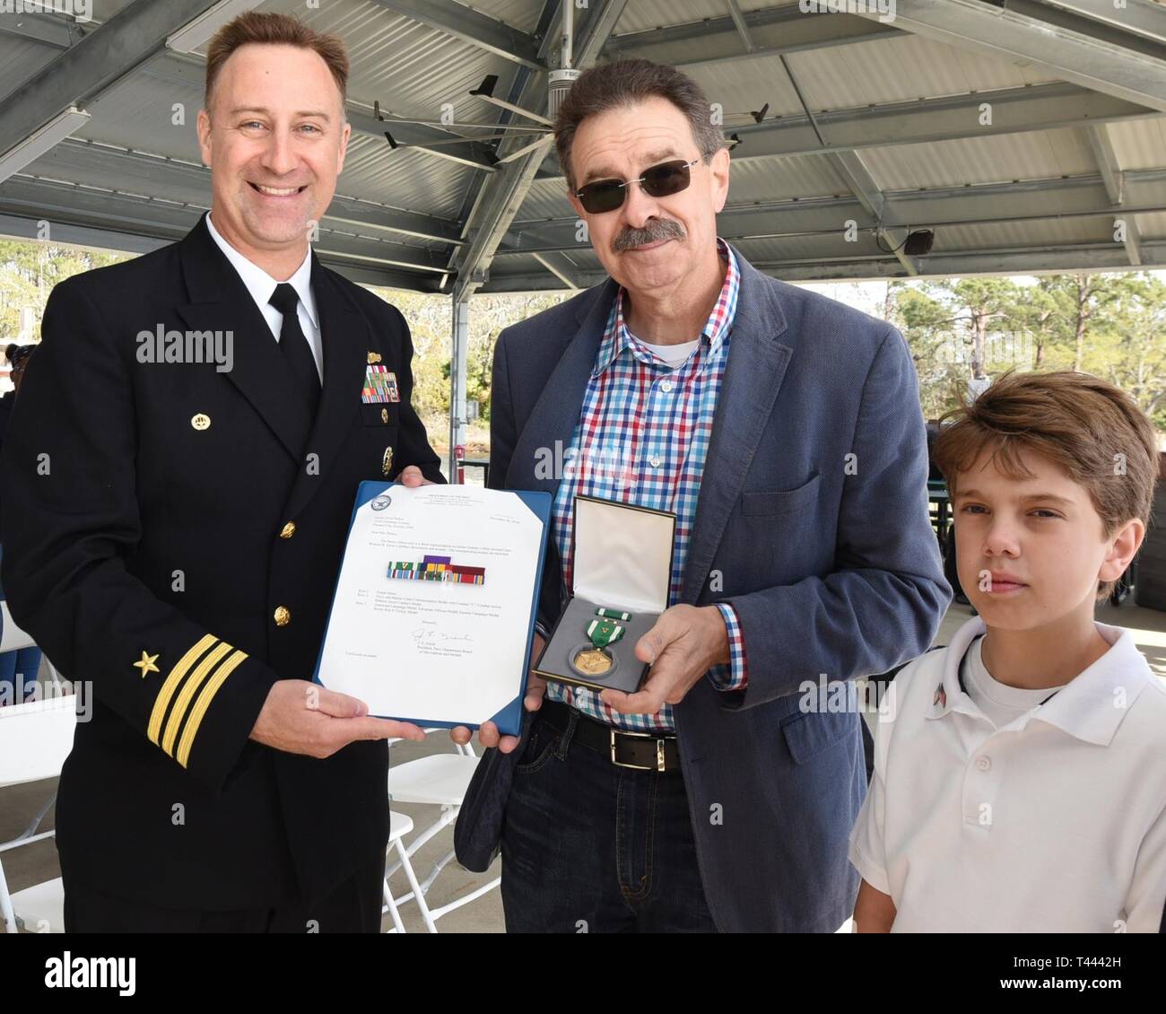Panama City, FL -- La base navale américaine de la ville de Panama commandant le Cmdr. Jay Sego présente Terry Parker, gendre de l'ancien combattant de la Seconde Guerre mondiale Gunner's Mate 2e classe Wheeler R. Ervin, le Navy-Marine Corps médaille avec vaillance au cours d'une cérémonie Jeudi, Mars 14, 2019. Également présents pour recevoir la médaille était petit-fils Kristopher Parker. En plus de la médaille de la famille, Ervin a également reçu la Purple Heart pour lutter contre les blessures qu'il a reçu à bord du Liberty Ship SS William W. Gerhard en août 1943. En tant que membre de la Marine de gardes armés dont la mission était de protéger la Banque D'Images