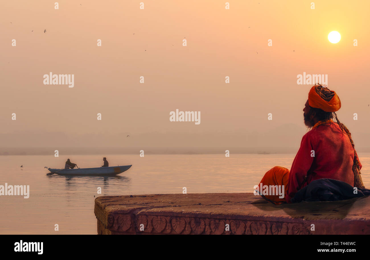 Hindu sadhu baba dans la méditation sur le Gange au lever du soleil avec vue sur la banque d'un bateau en bois sur le fleuve Ganga Banque D'Images