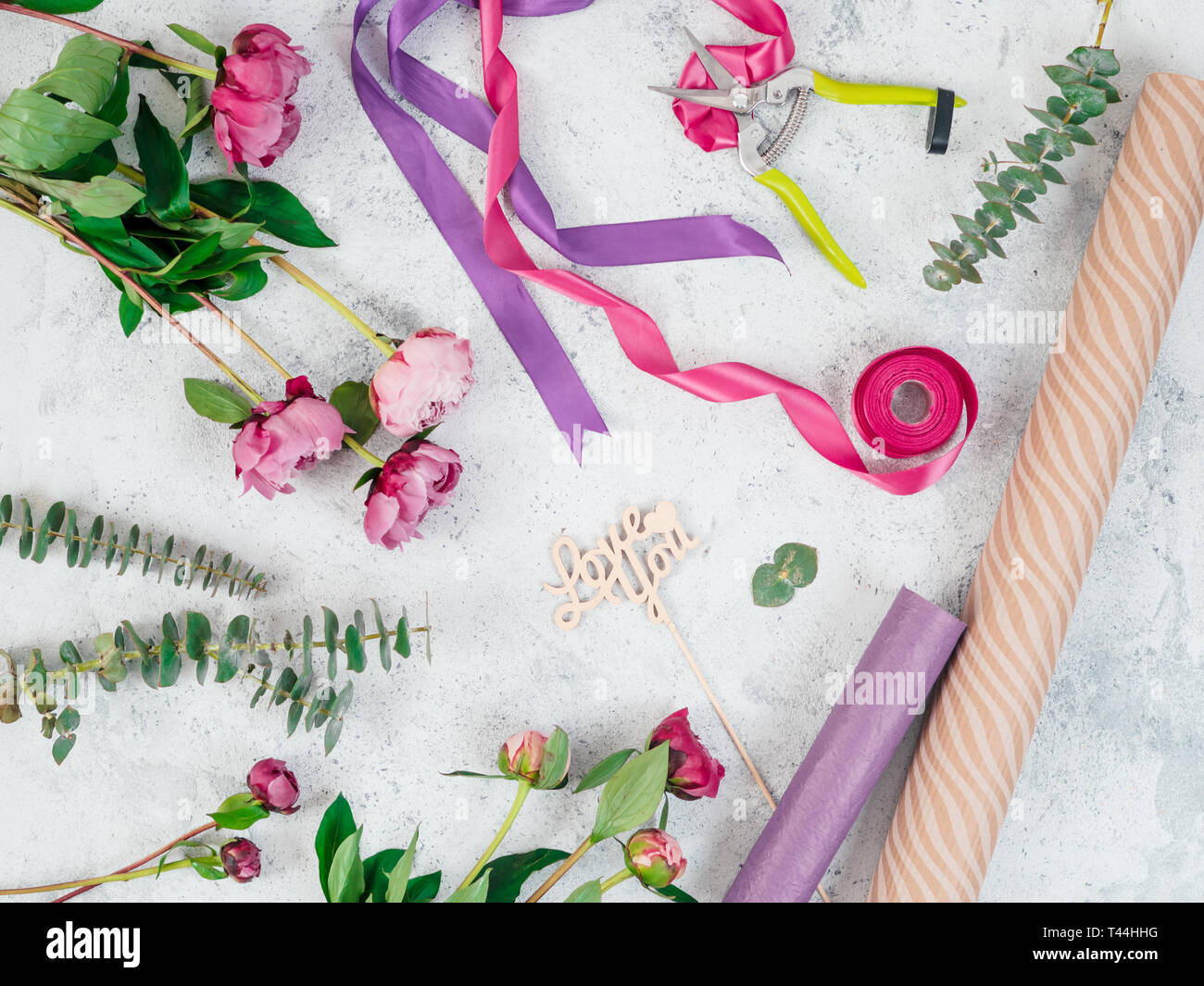 Télévision floristique lay. Des fleurs, du papier d'emballage, rubans et de l'amour vous panneau en bois gris sur la table. Roses, eucalyptus, copiez l'espace. Pouvez utiliser les médias sociaux de l'affichage Banque D'Images