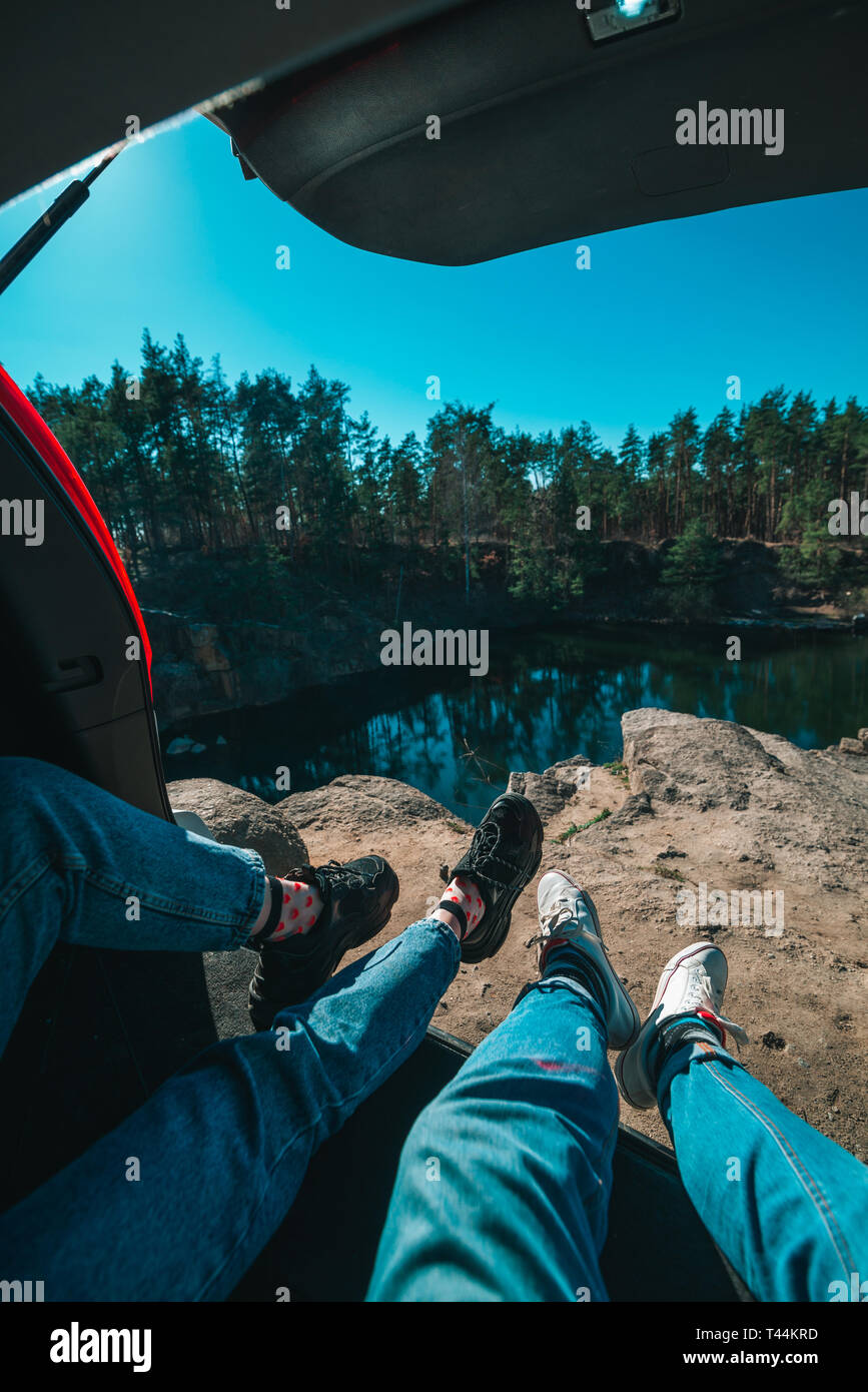 Couple sitting in car trunk lac sur l'arrière-plan. jambes en baskets et jeans. travel concept Banque D'Images
