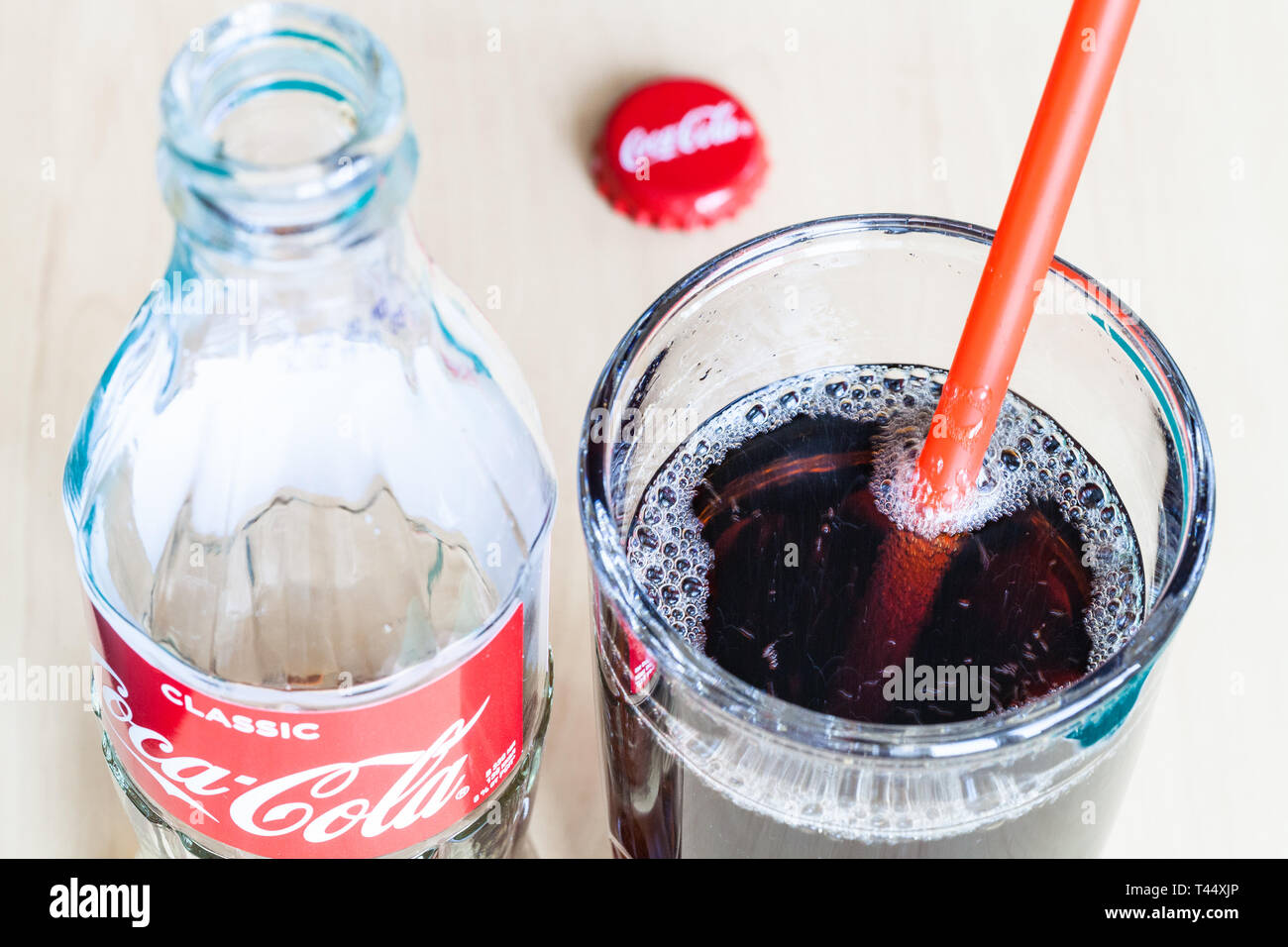 Moscou, Russie - le 4 avril 2019 : boire en verre avec paille rouge et vide bouteille de Coca-Cola boissons sur la table. Coca-Cola (coke) gazéifiée Banque D'Images