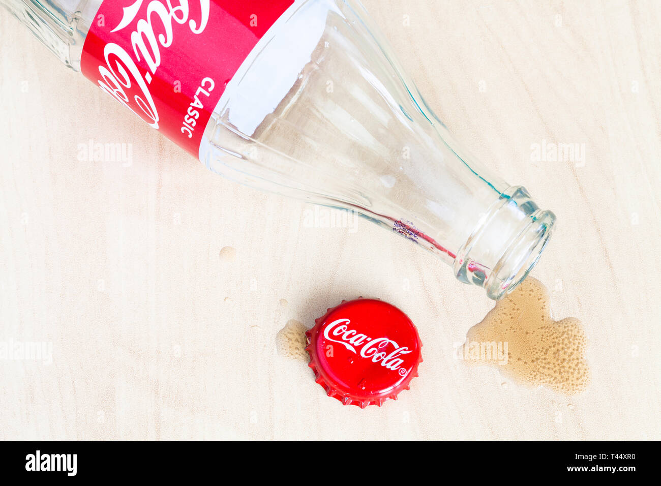 Moscou, Russie - le 4 avril 2019 : cap Couronne, bouteille vide de boisson Coca-Cola renversé et flaque sur planche de bois. Coca-Cola (coke) carbonate est Banque D'Images