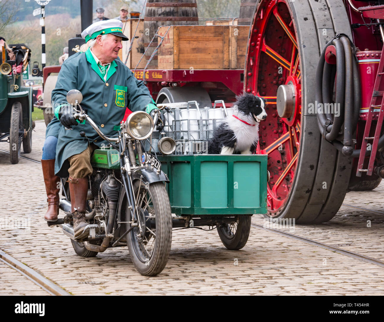 Beamish Museum, Beamish, comté de Durham, Angleterre, Royaume-Uni, 13 avril 2019. Beamish jour vapeur : Senior homme habillé en costume d'époque ou le laitier Laitier conduisant un vintage 1925 Royal Enfield moto avec collie dog et la bouteille de lait en side-car sur l'affichage à l'Beamish Musée Vivant Banque D'Images