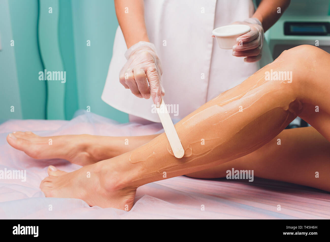 L'esthéticienne est la préparation pour l'épilation et l'application de la  crème avec de la cire stick sur la belle femme aux jambes. Salon de beauté  Photo Stock - Alamy