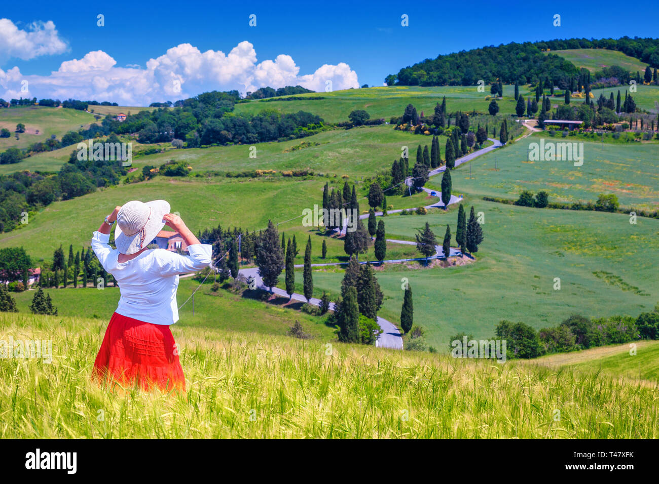 Tourist femme dans une jupe rouge chemise blanche et un chapeau de paille en admirant la vue sur la Toscane. Lieu touristique rural bien connu avec des champs de céréales un Banque D'Images