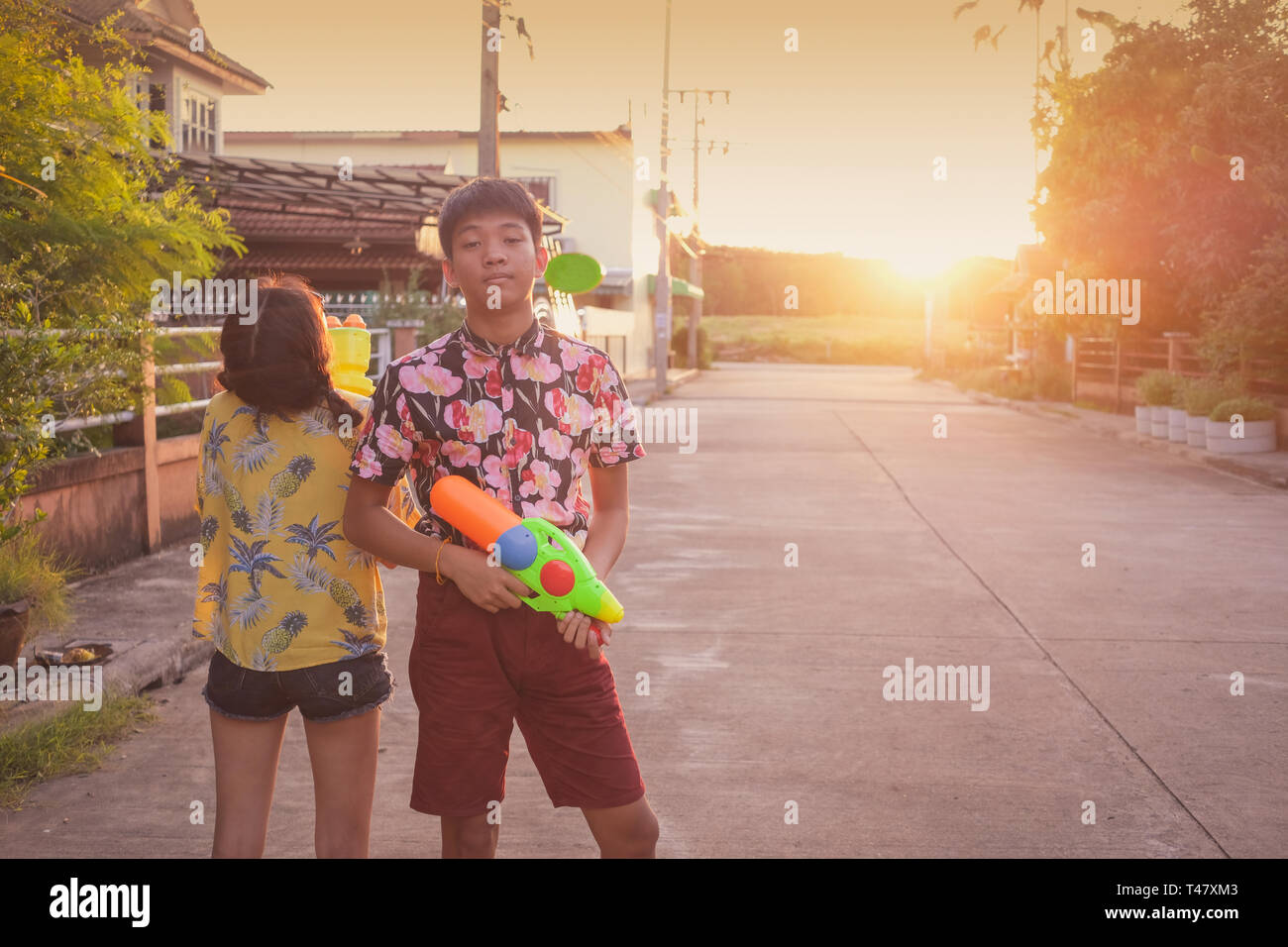Garçon et fille jouer ensemble sur des armes à feu de l'eau festival de Songkran en Thaïlande au cours de coucher du soleil fond de scène Banque D'Images