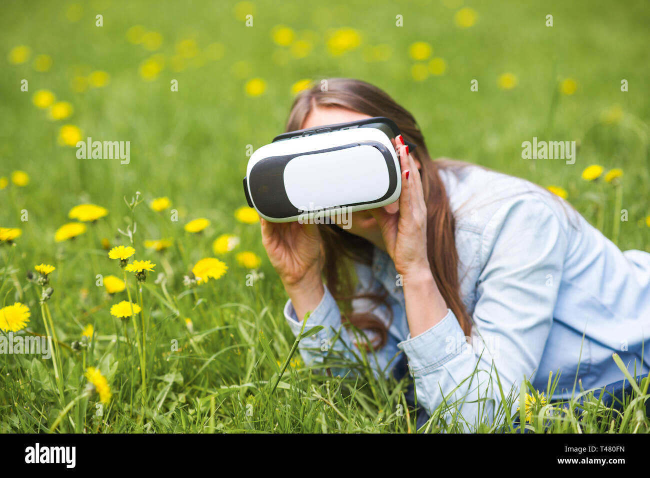 Femme à l'aide du casque de réalité virtuelle à l'extérieur pose en champ de fleurs de printemps Banque D'Images