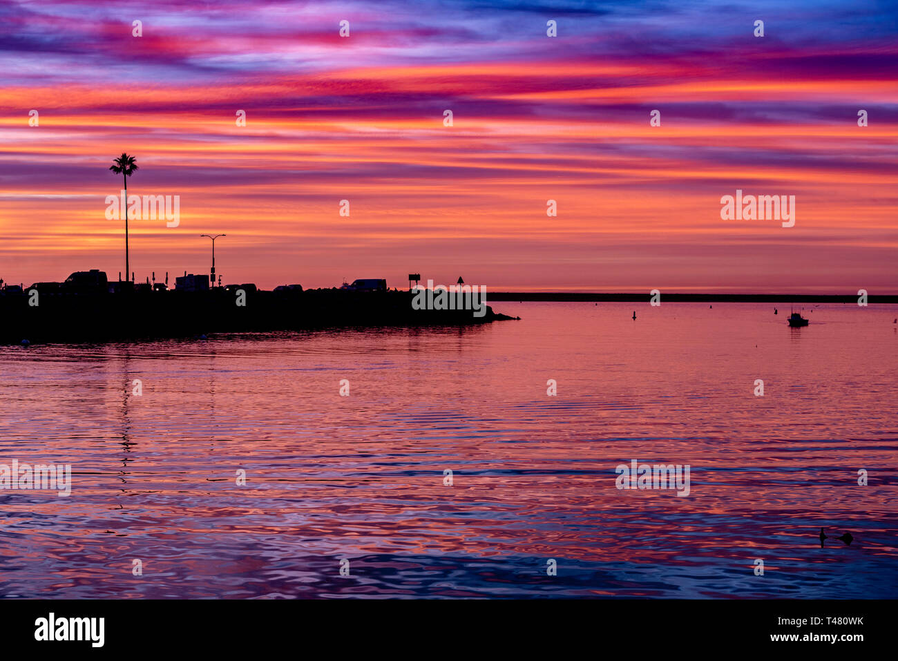 Silhouette d'une île contre l'Ciel de coucher du soleil. L'océan est ce qui reflète les couleurs du ciel, bleu, rouge, jaune et orang. Banque D'Images