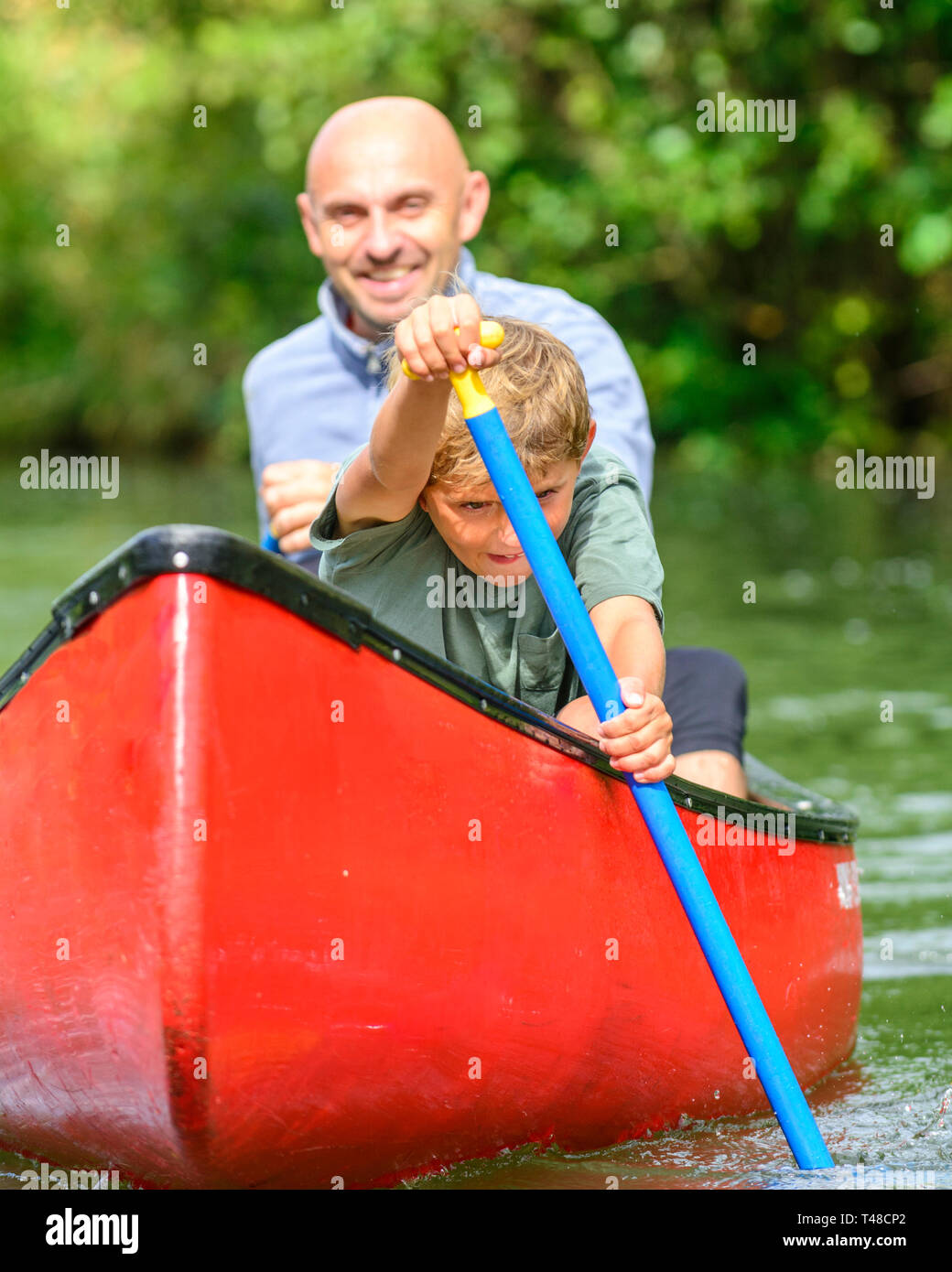 Jeune garçon avec impatience la pagaie avec son père en canoe Banque D'Images