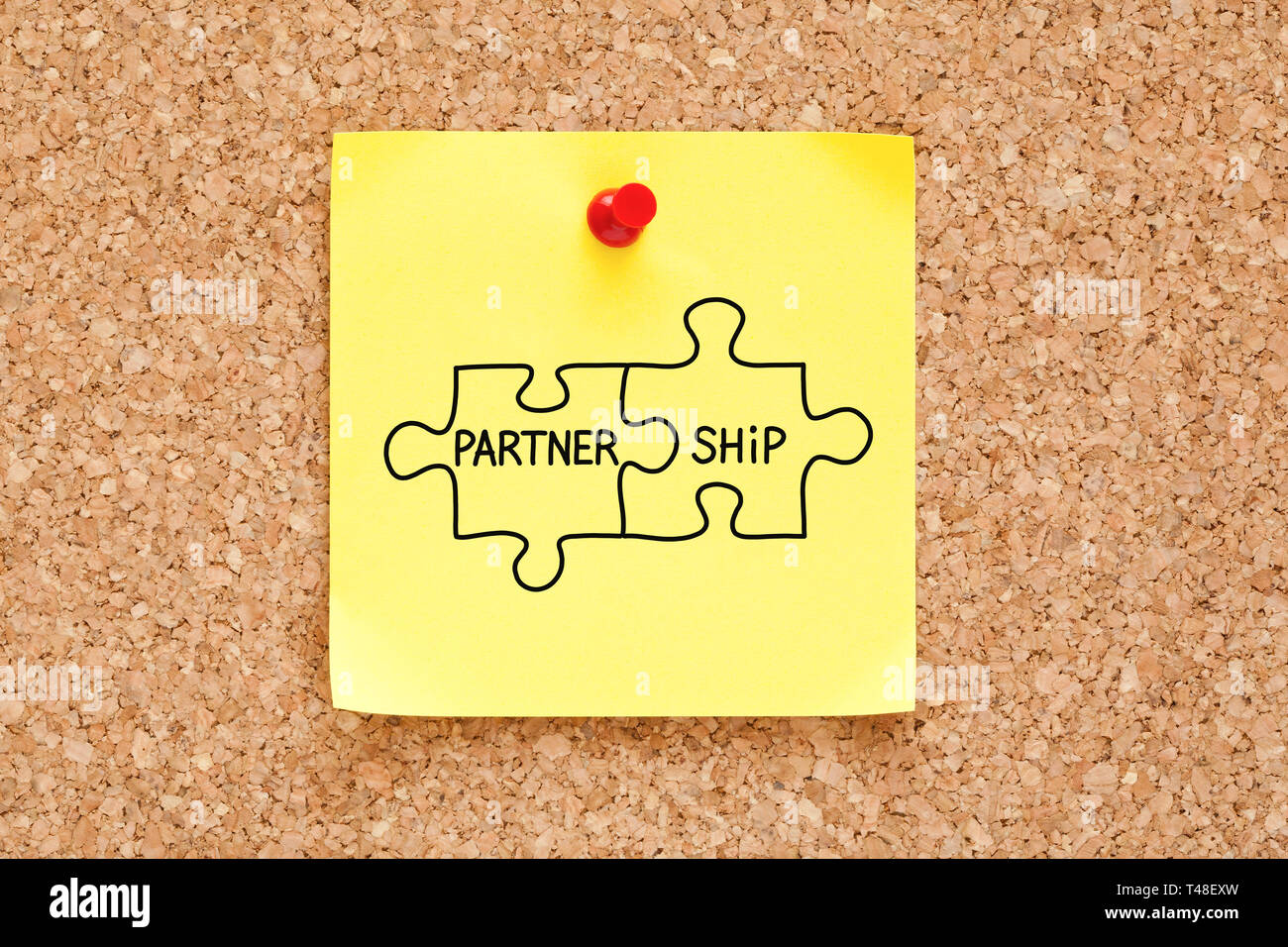 Concept de partenariat puzzle à la main sur yellow sticky note épinglée sur panneau de liège. Banque D'Images