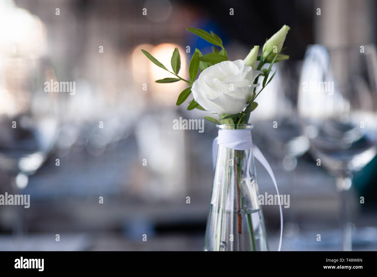 Vase en verre transparent avec bouquet de fleurs contre l'arrière-plan de la table, dans un restaurant moderne. Vin et verres à eau stand dans la rangée de maisons Banque D'Images