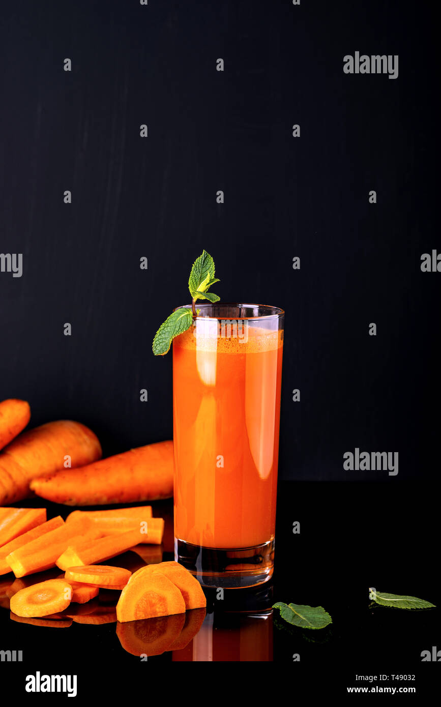 Verre de jus de carotte avec quelques morceaux de carotte sur un fond noir. La carotte crue verre Banque D'Images