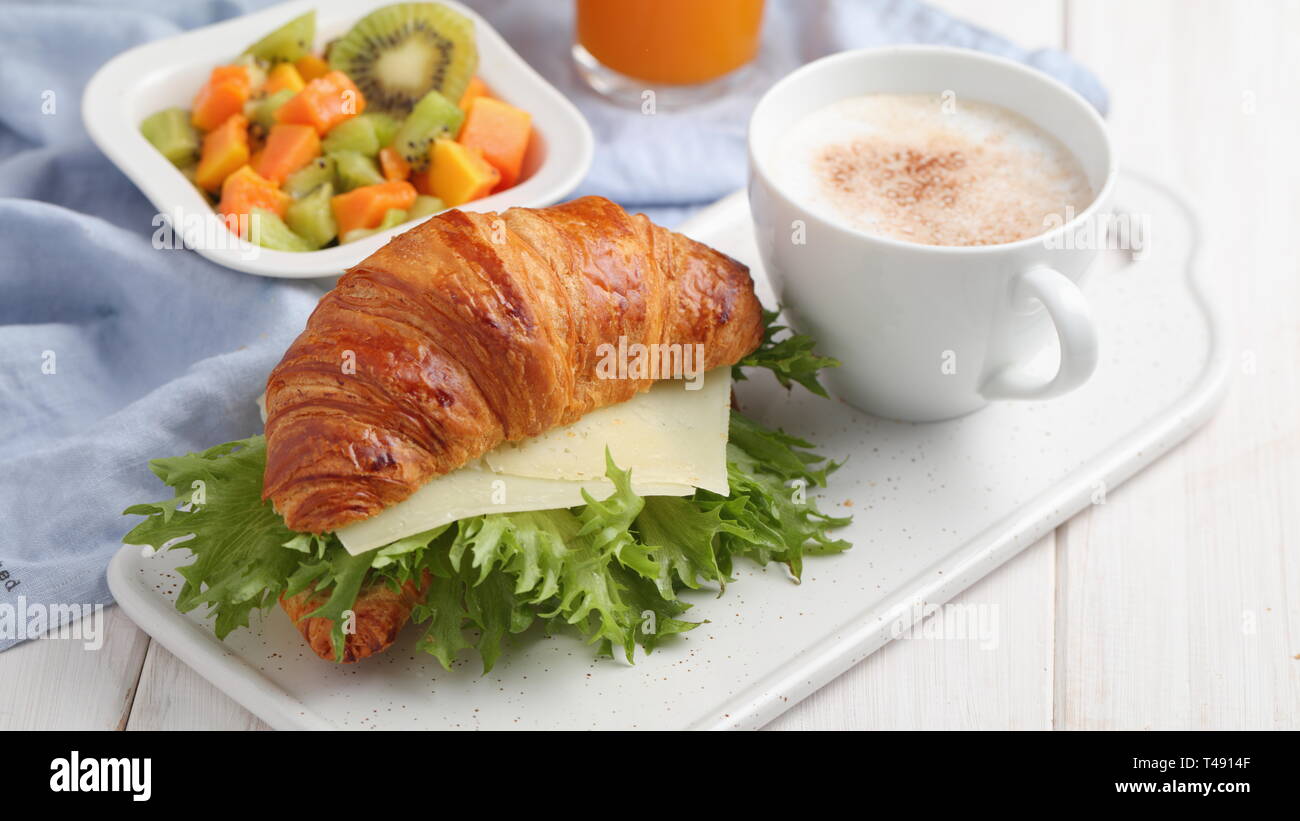 Petit-déjeuner français : croissant sandwich avec du fromage, salade de fruits, et une tasse de cappuccino Banque D'Images