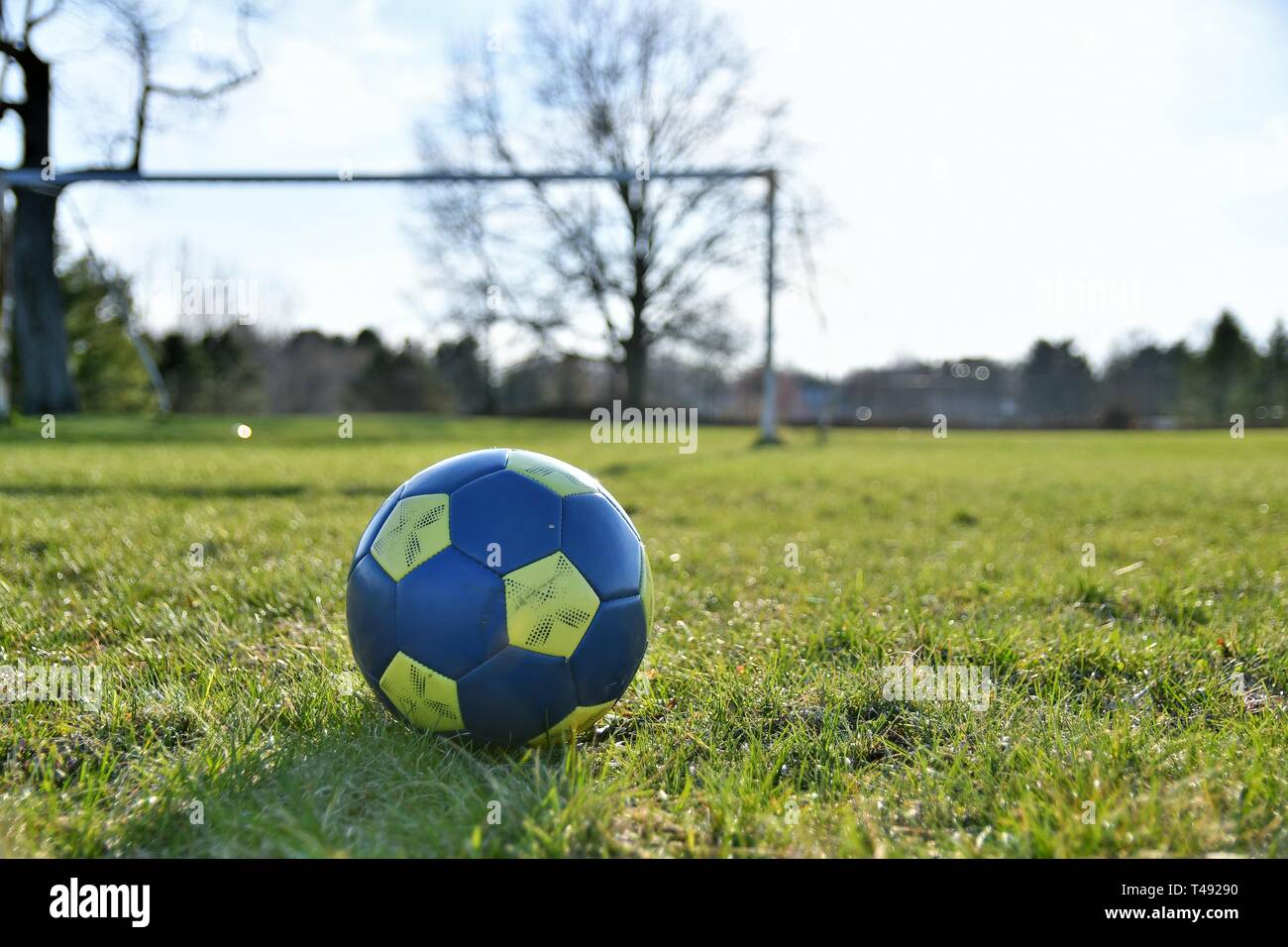 Close up d'un ballon de soccer bleu et jaune au printemps avec un champ et de buts de soccer à l'arrière-plan Banque D'Images