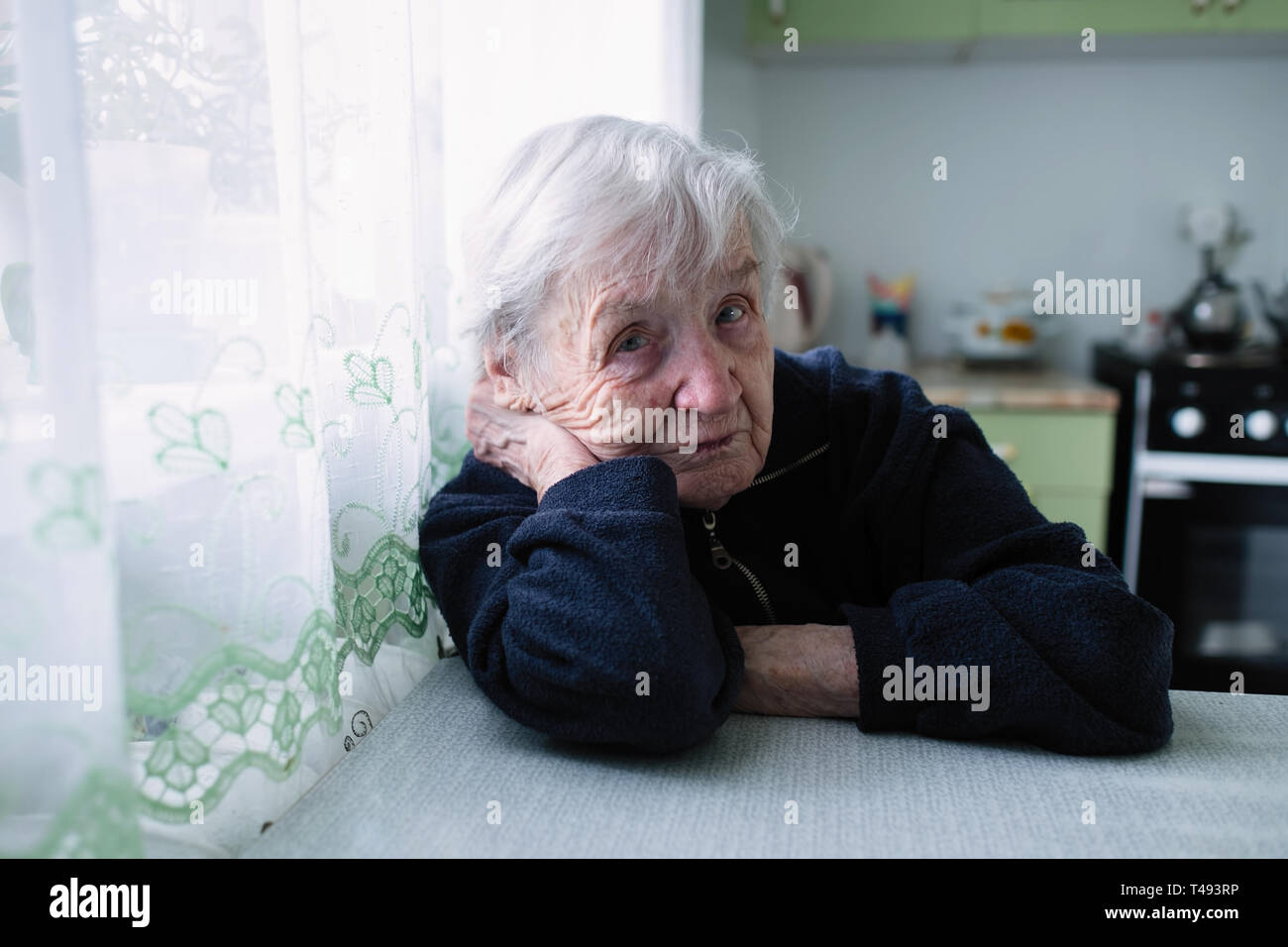 Portrait d'une vieille femme assise dans la cuisine de son appartement. Banque D'Images