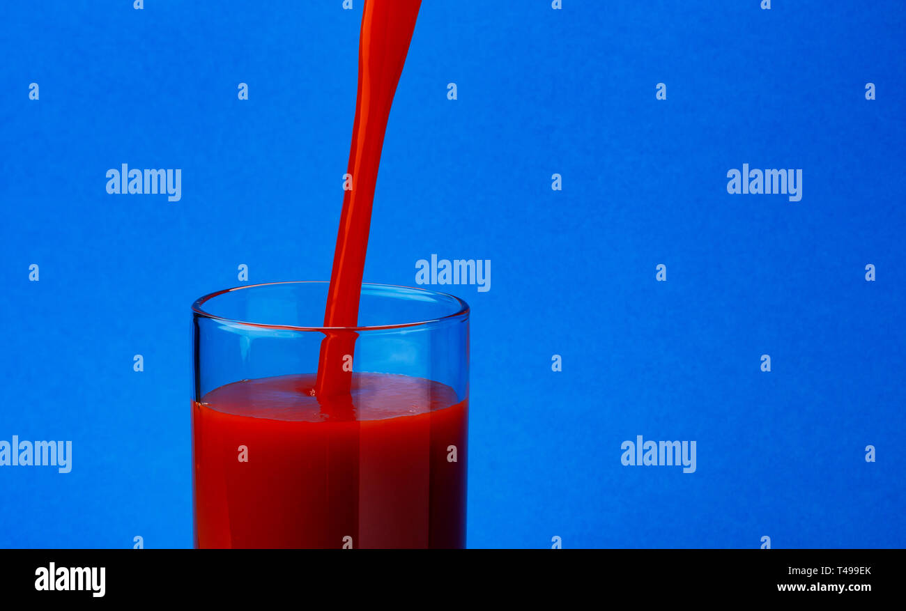 Les jus de tomates et verser dans le verre, isolé sur fond bleu, avec copie espace Banque D'Images