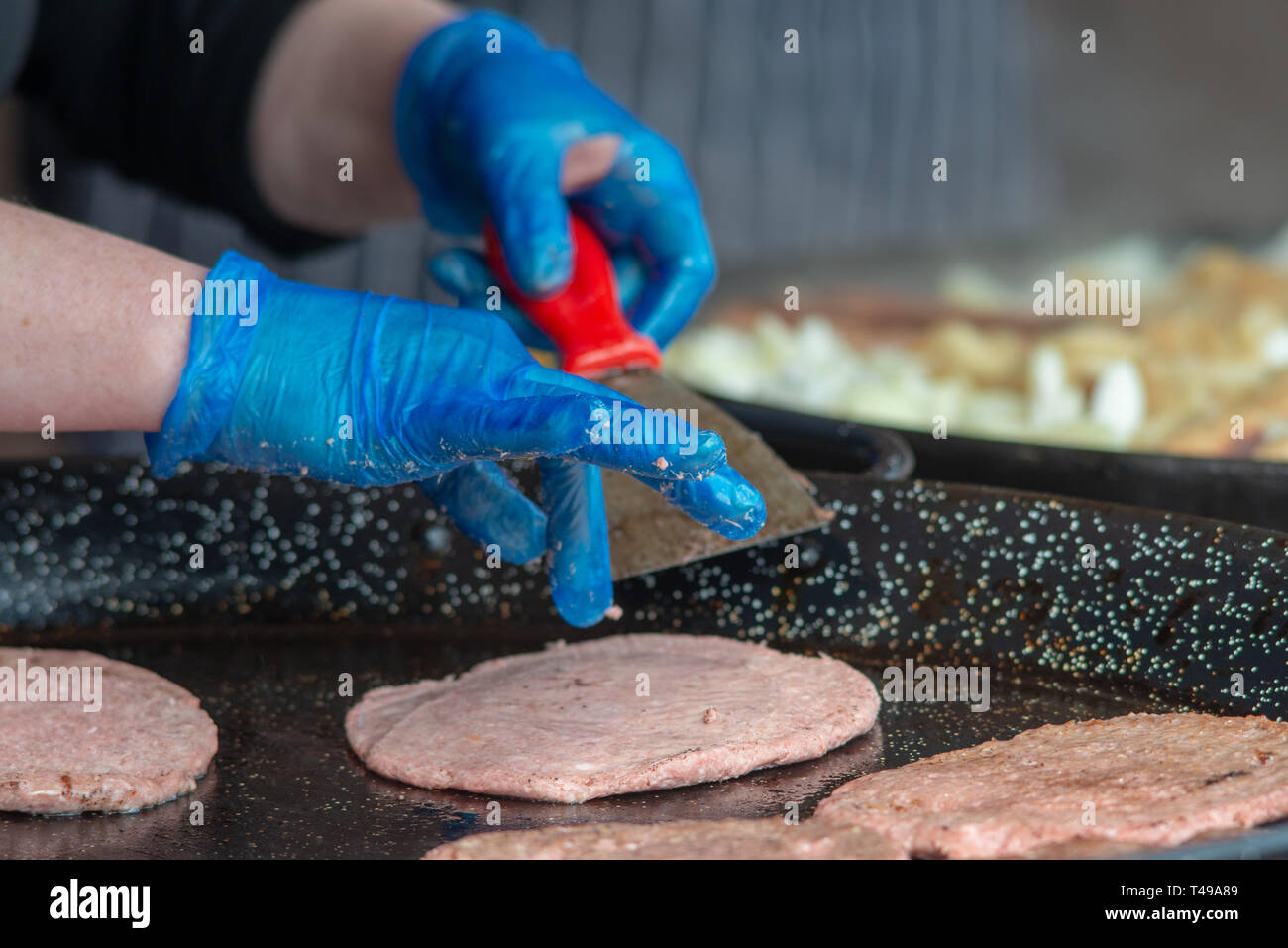 La cuisson des hamburgers sur une crêpière portant des gants bleu pour répondre aux normes d'hygiène alimentaire Banque D'Images