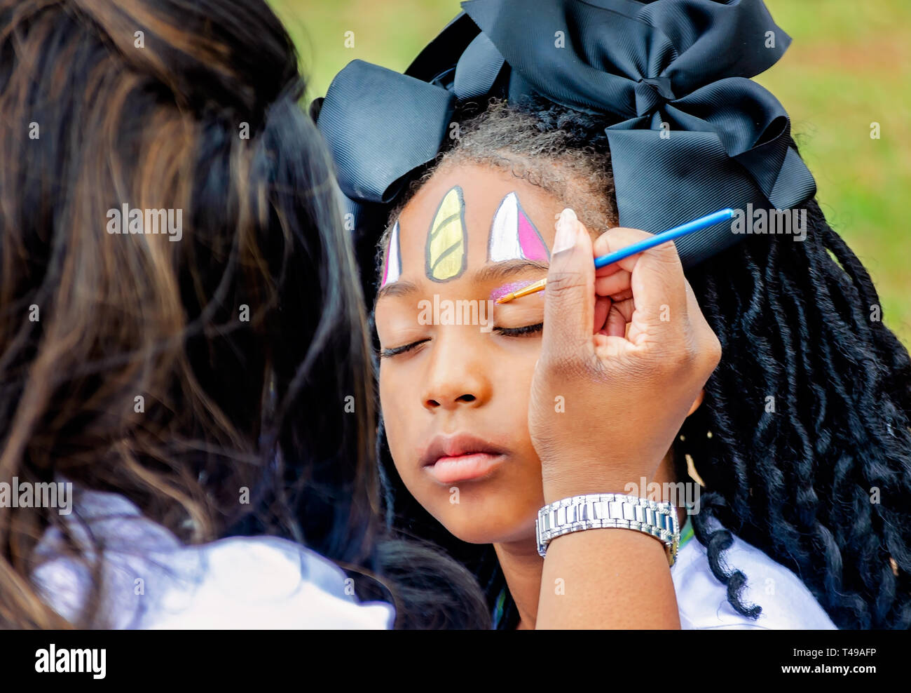 Une fille ferme les yeux comme un peintre face s'applique l'ombre d'oeil pendant une chasse aux œufs de Pâques à Langan Park, le 13 avril 2019, à Mobile, Alabama. Banque D'Images