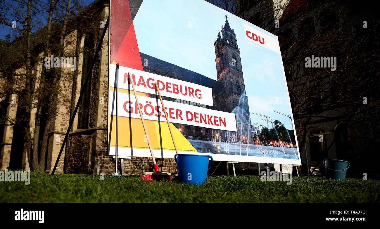 Magdeburg, Allemagne. Apr 15, 2019. Balais et seaux sont debout devant une affiche électorale avec l'inscription 'Magdeburg voir plus grand' au début de la campagne électorale officielle l'affichage de la CDU dans le Land de Saxe-Anhalt. Credit : Ronny Hartmann/dpa-Zentralbild/ZB/dpa/Alamy Live News Banque D'Images