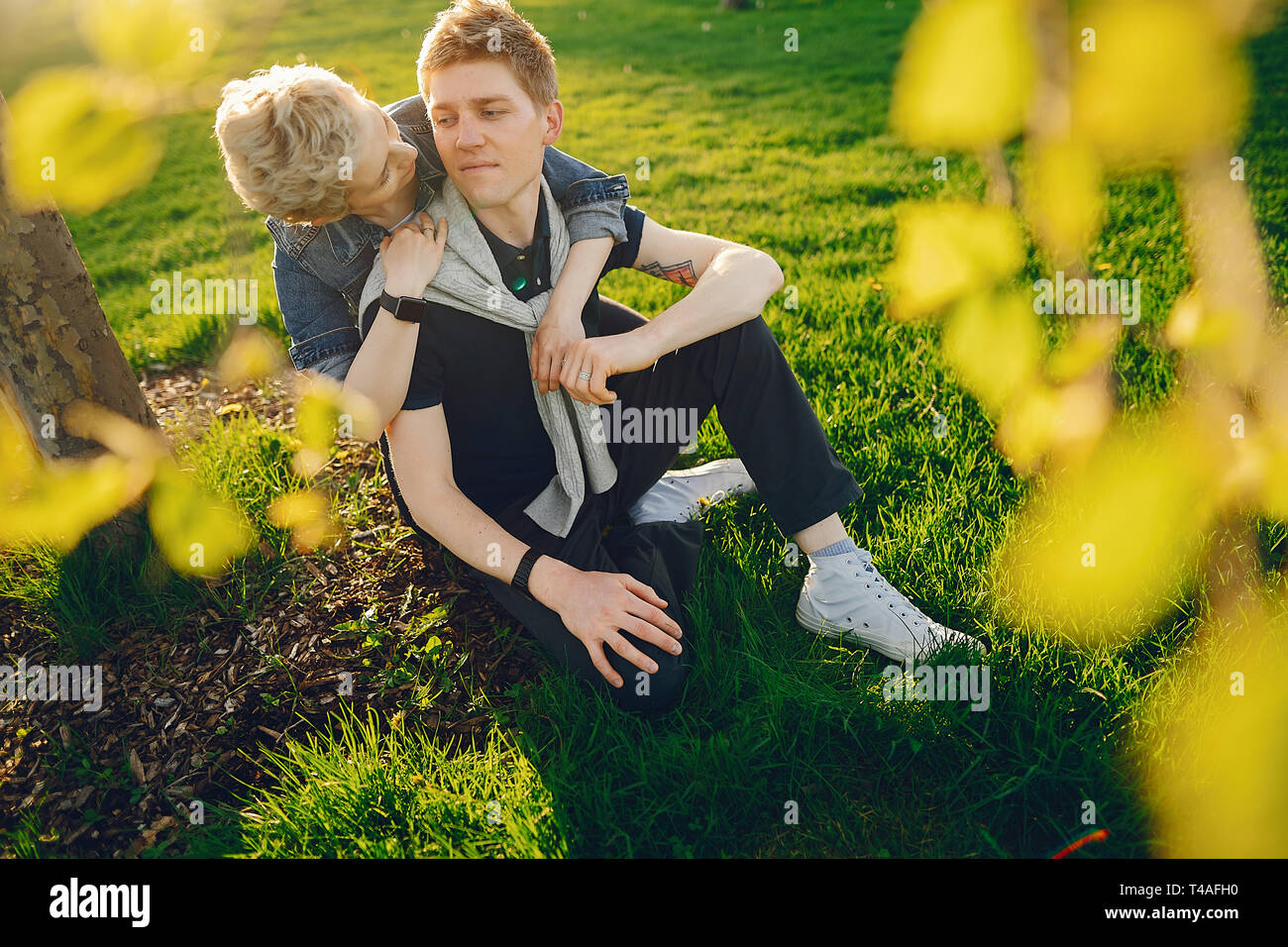 Femme élégante et belle avec les cheveux courts, vêtu d'une veste bleu jeans avec son bel homme assis dans un parc verdoyant ensoleillé Banque D'Images