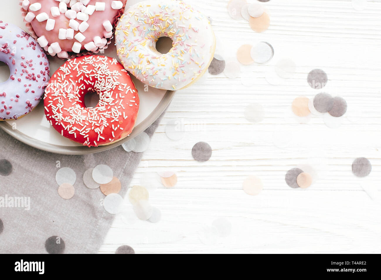 Délicieux donuts colorés avec sprinkles sur plaque sur le tableau blanc élégant avec confetti, télévision lay. Partie concept. Pas de régime alimentaire. Candy bar at wedding recepti Banque D'Images