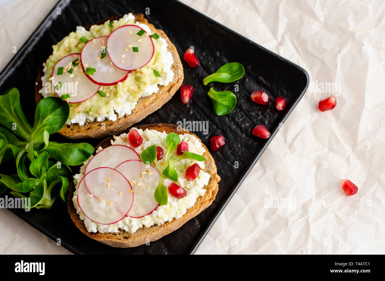 Des toasts avec du fromage cottage et brisé l'avocat, radis, salade de maïs et de plantes graines de grenade sur la plaque noire. Vue d'en haut. Copier l'espace. Une saine alimentation Banque D'Images