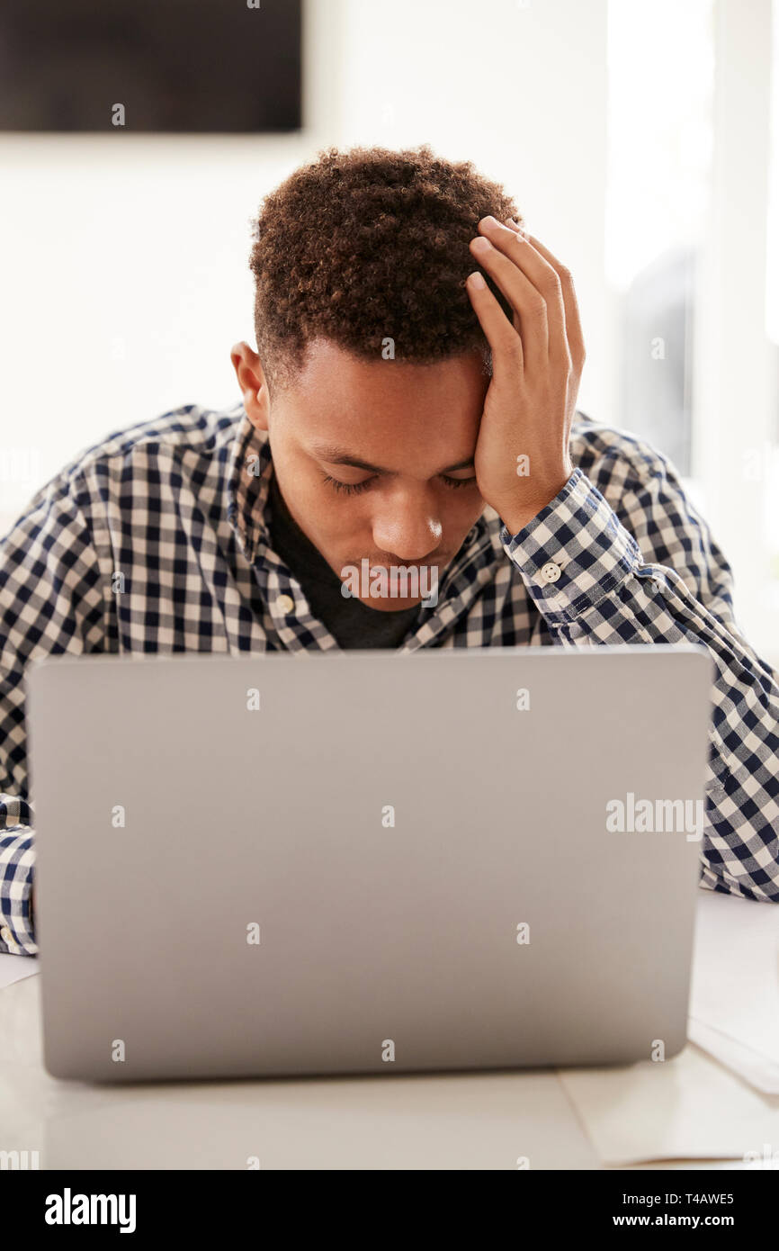 Black Boy déprimé avec la tête dans les mains à l'aide d'un ordinateur portable à la maison, vertical Banque D'Images