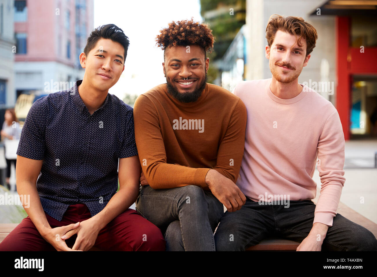 Trois amis hipster homme millénaire sur un banc dans une rue de ville souriant pour appareil photo, Close up Banque D'Images