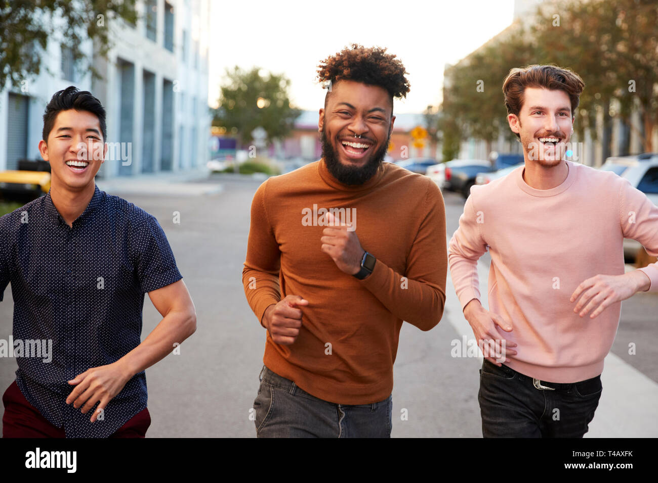 Les jeunes adultes de sexe masculin de la hanche trois amis courir pour le plaisir dans une ville road, vue de face, Close up Banque D'Images