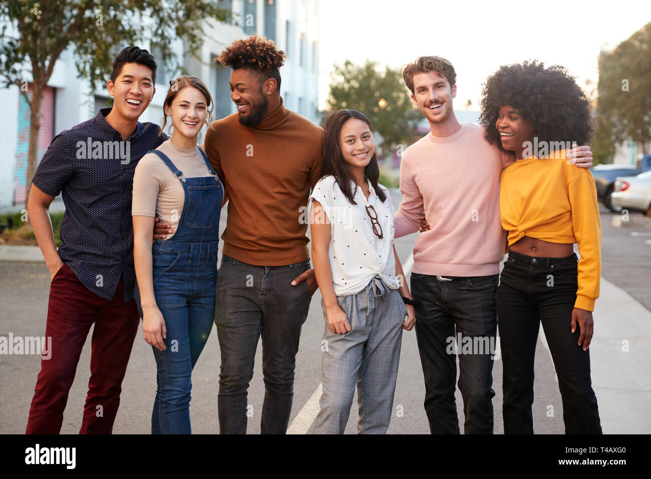 Six amis hipster millénaire debout dans une rue de ville souriant pour appareil photo, trois quarts Banque D'Images