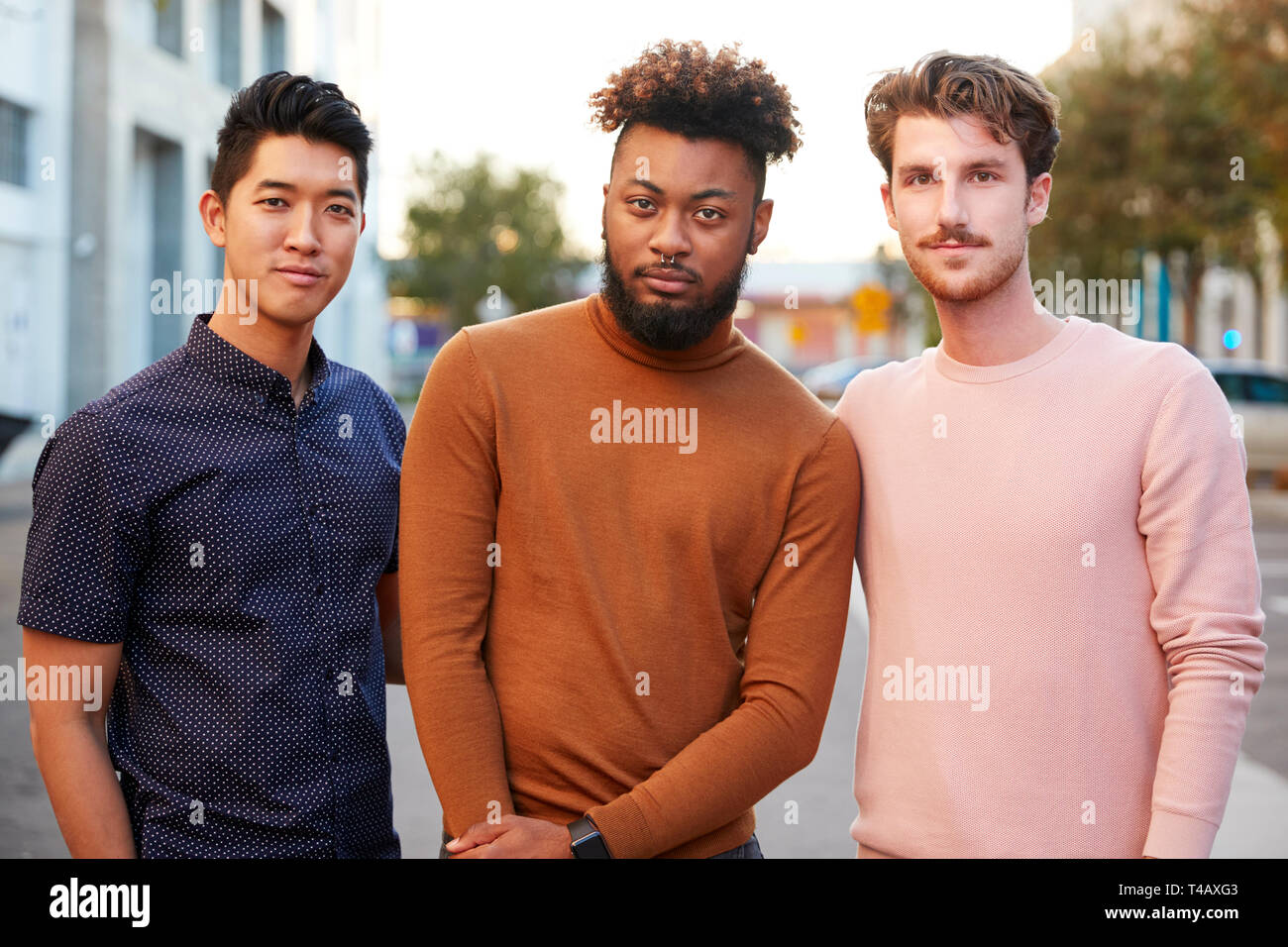 Les jeunes adultes de sexe masculin de la hanche trois amis debout dans une rue de la ville à la recherche d'appareil photo, vue de face, Close up Banque D'Images